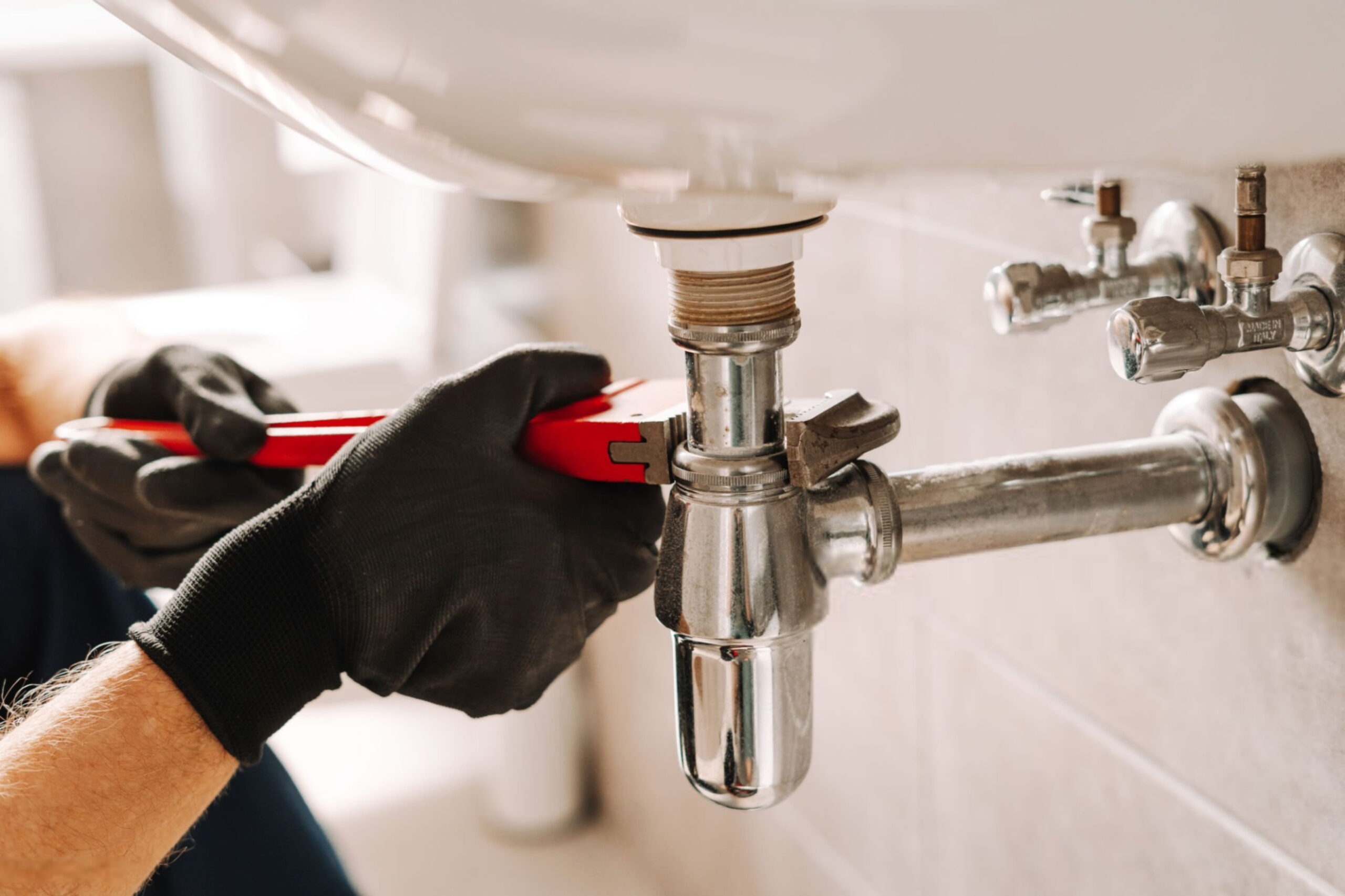 Plumber using adjustable wrench for repairing sink pipe